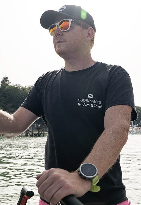 A man in a black t-shirt and baseball cap driving a small boat